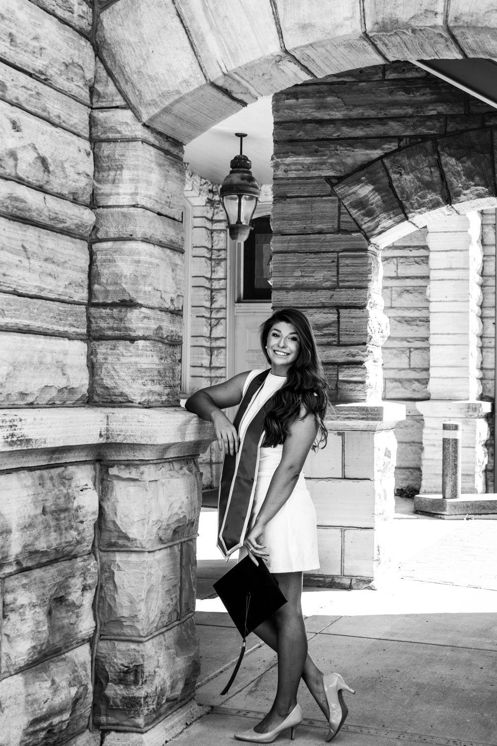 A black and white graduation photo captured under a stone archway with vintage lantern.