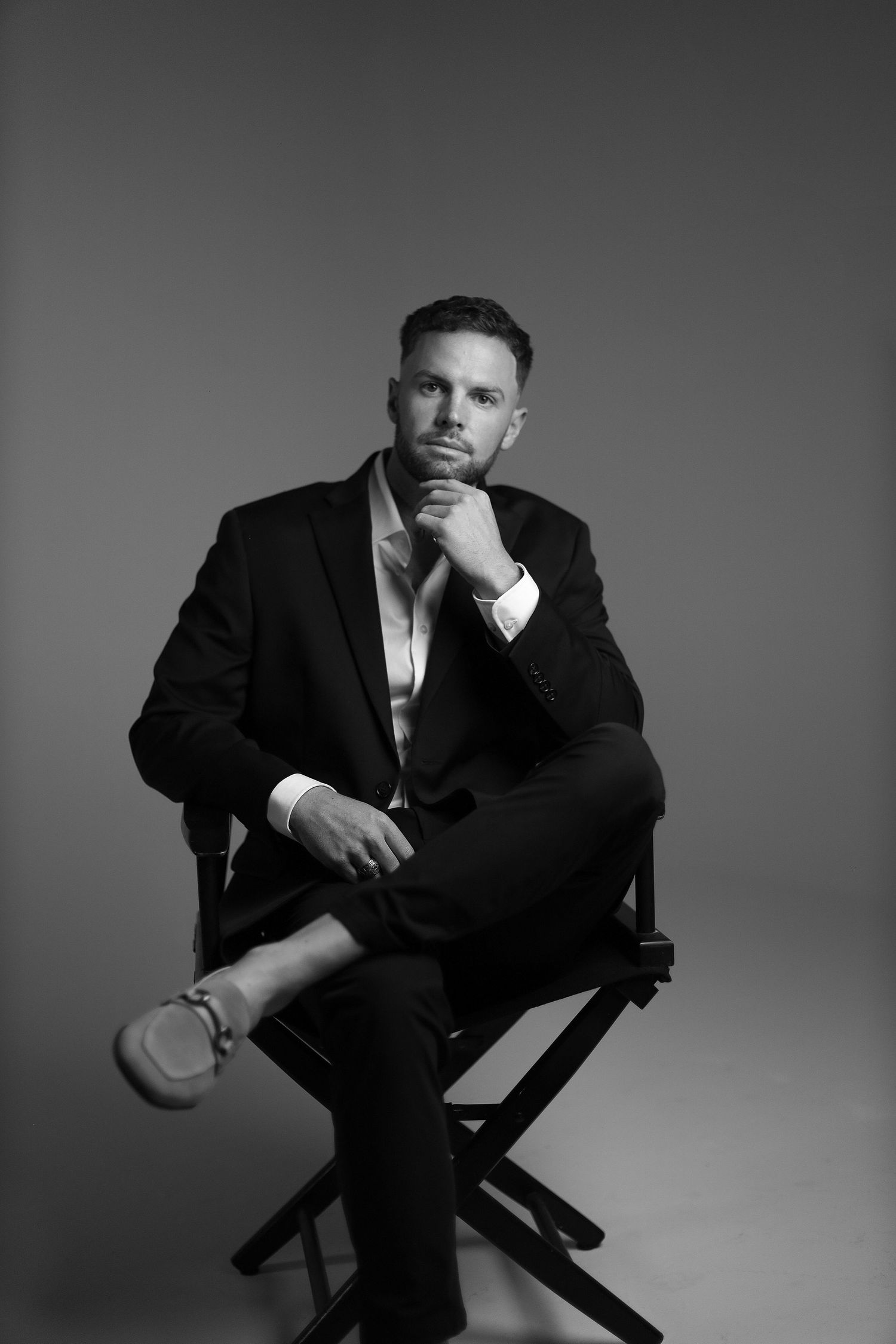 Black and white portrait of a model in formal suit sitting thoughtfully on director's chair.