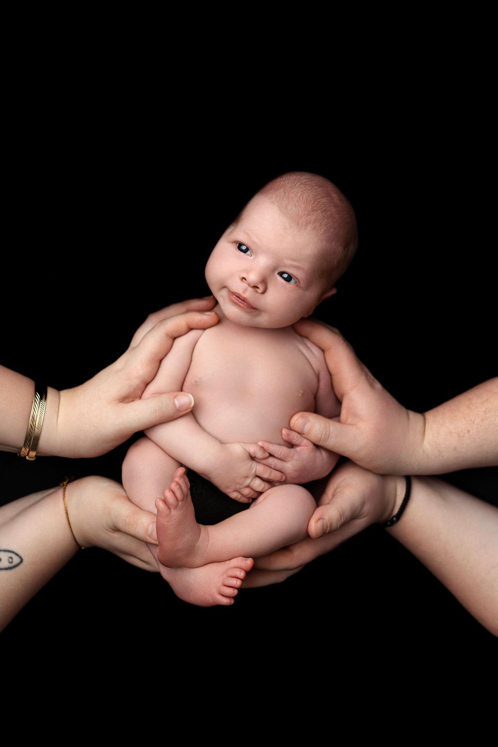 A series of four artistic black and white photos showing adult hands gently cradling a newborn baby against a dark background.
