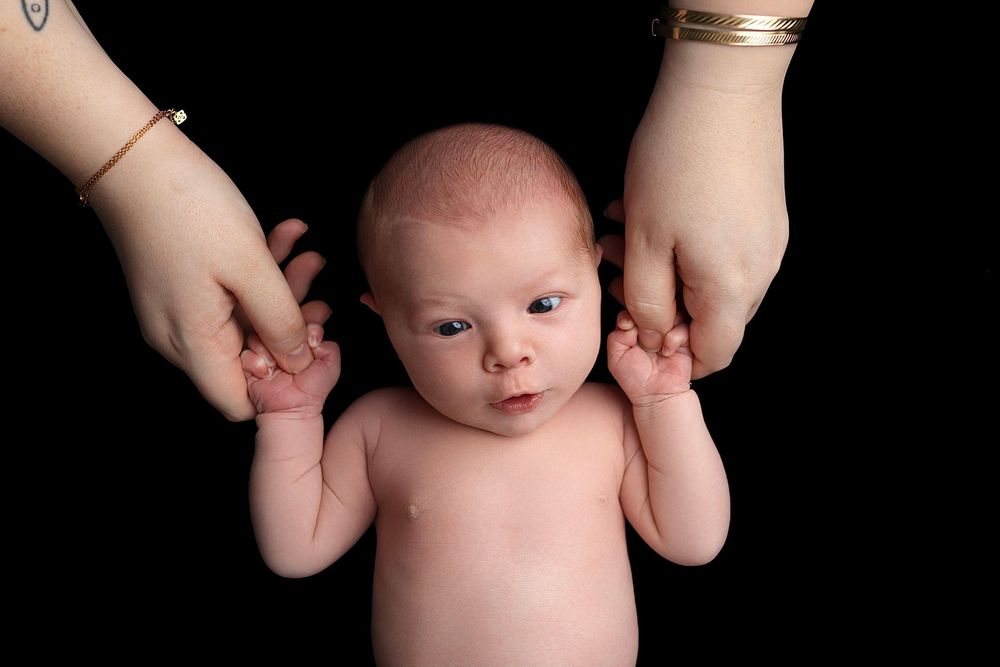 A newborn baby's torso is gently supported by adult hands against a dark background.