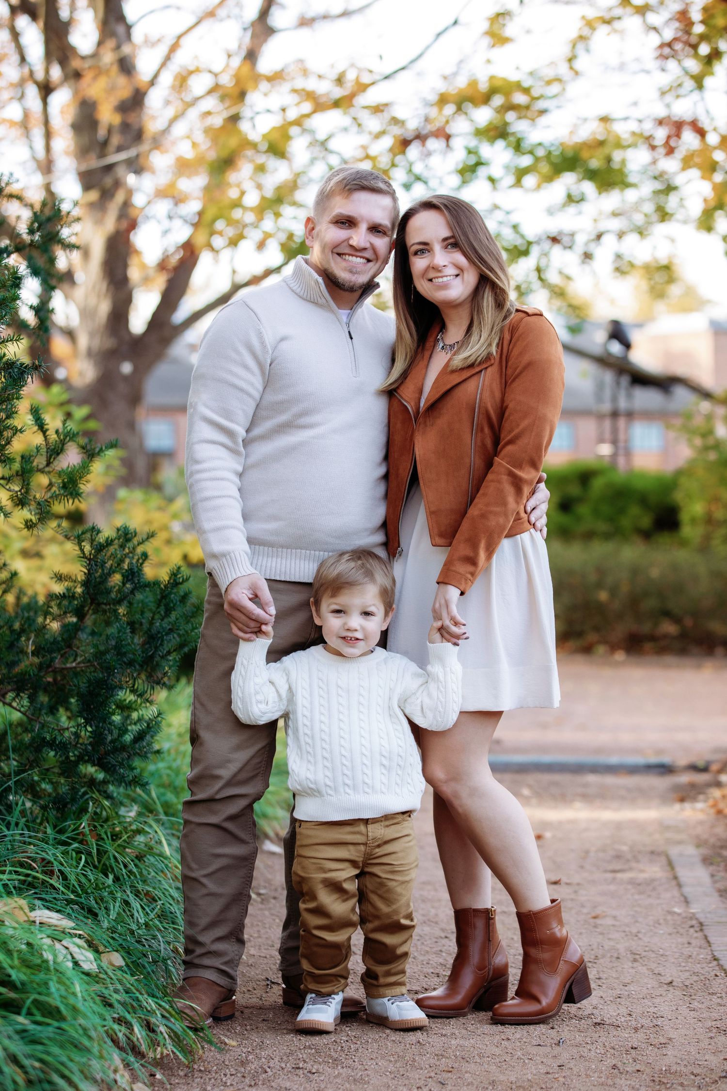 A family dressed in cozy autumn attire poses together on a path surrounded by fall foliage.