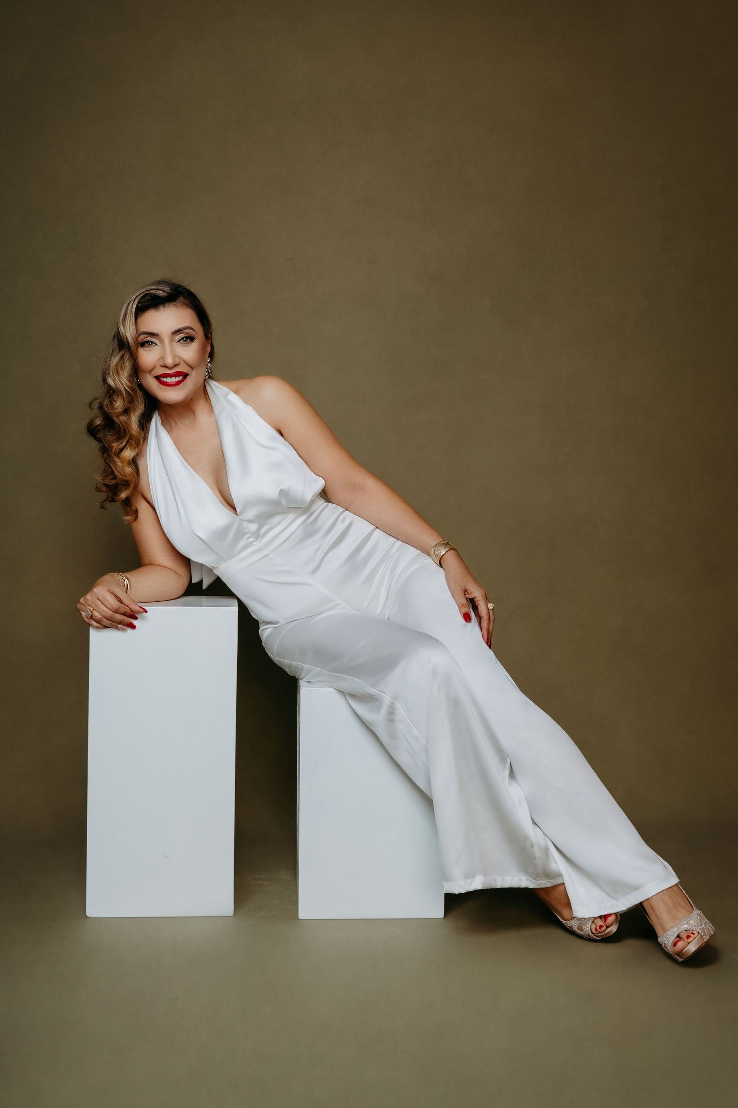 Woman in elegant white jumpsuit poses gracefully on geometric blocks.