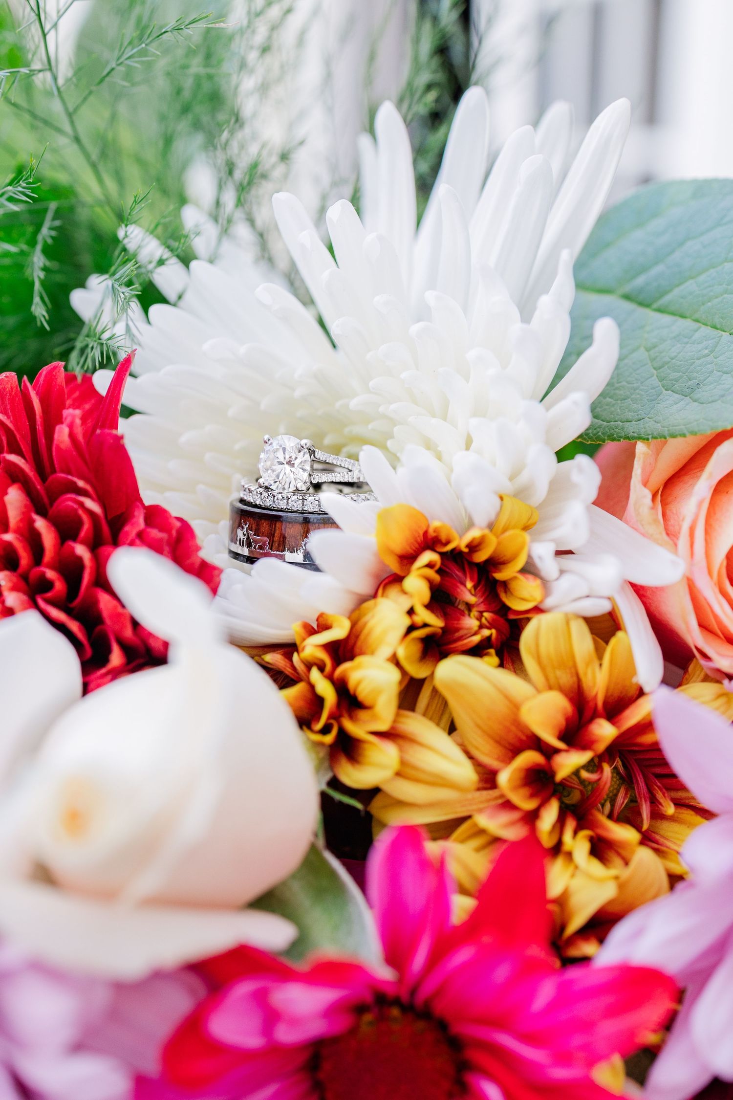 Wedding rings nestled among colorful autumn flowers including dahlias and roses.