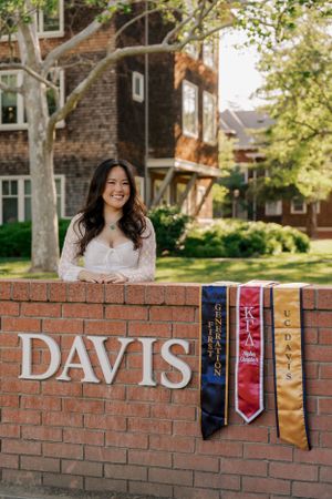 A brick wall with 'DAVIS' text and decorative graduation stoles hanging at a university campus on a sunny day.