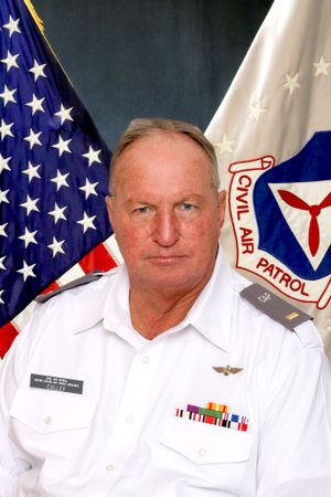 Civil Air Patrol officer in white uniform poses with American flag and organizational emblem.