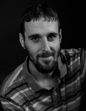Black and white portrait of person wearing striped shirt against dark background.