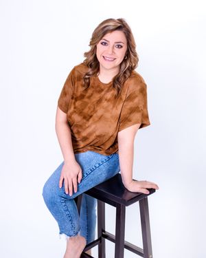 A person in a brown t-shirt and jeans sits casually on a dark wooden barstool against a white backdrop.