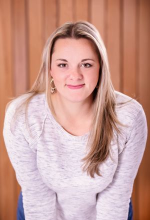 Portrait of person in white sweater with long blonde hair against wooden background.