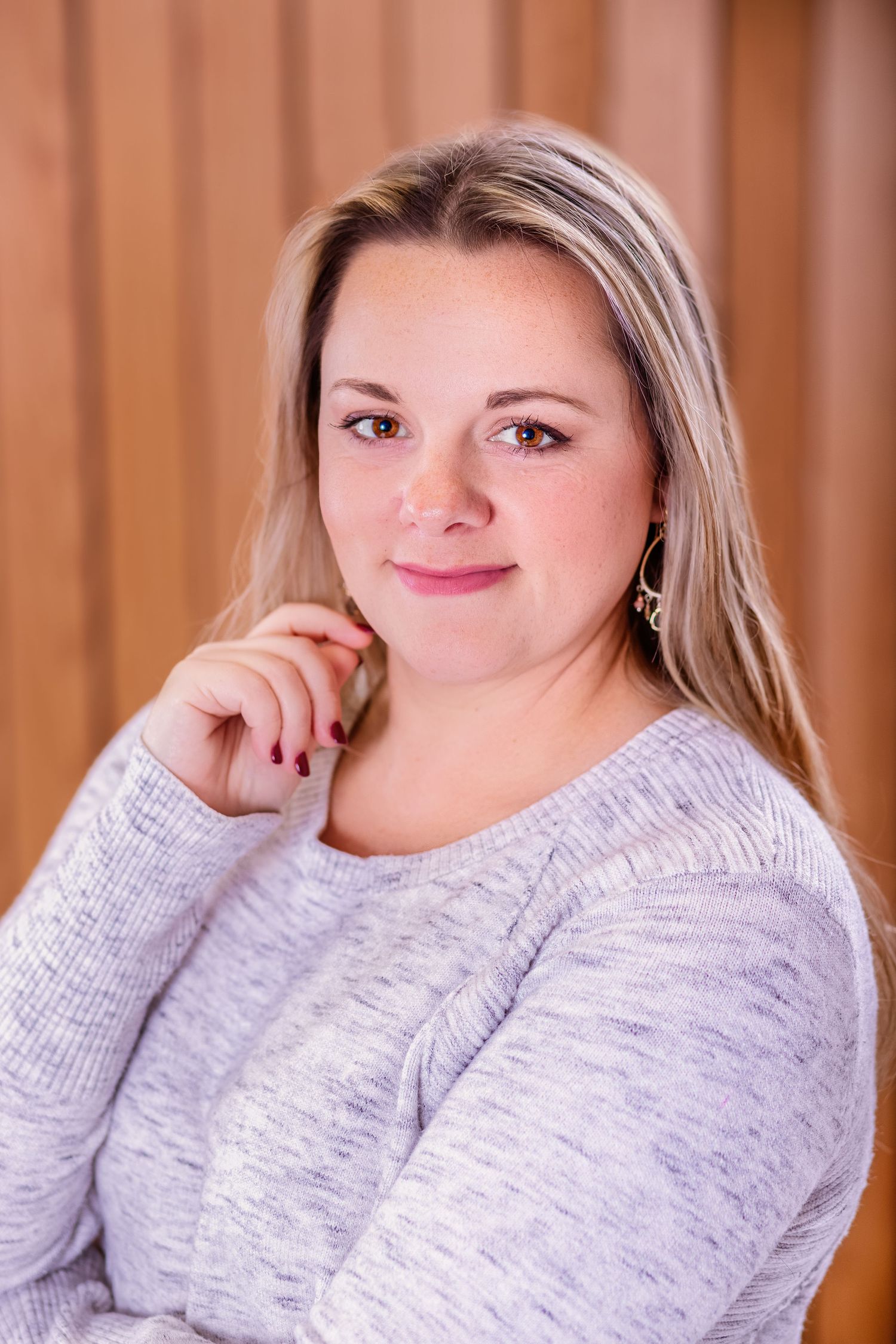 Portrait of person in gray sweater with blonde hair against warm-toned background.