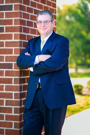 Professional in navy suit poses confidently against brick wall outdoors.