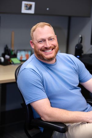 A person in a light blue t-shirt sits at a desk smiling warmly in a series of connected photos.
