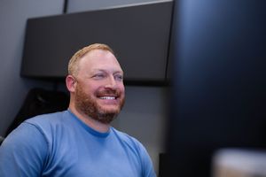 Man wearing a blue shirt smiles while looking to the side in a professional headshot-style photo.