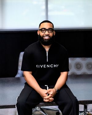 A person wearing a black Givenchy t-shirt sits in a chair during what appears to be an interview or presentation setting.