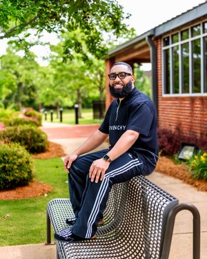 Person wearing Givenchy apparel sits casually on outdoor mesh bench in garden setting.