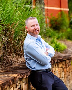 Professional portrait session outdoors on stone wall with natural greenery in background.