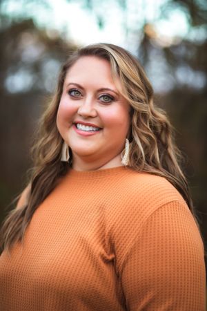Portrait of person in orange sweater with wavy hair and tassel earrings.