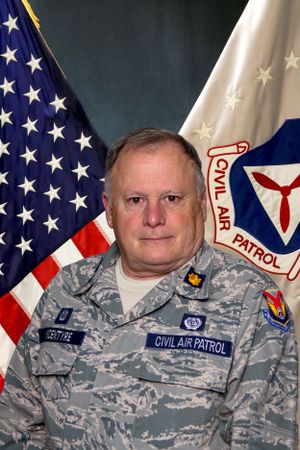 Civil Air Patrol officer in digital camouflage uniform poses for official photo with American and CAP flags.