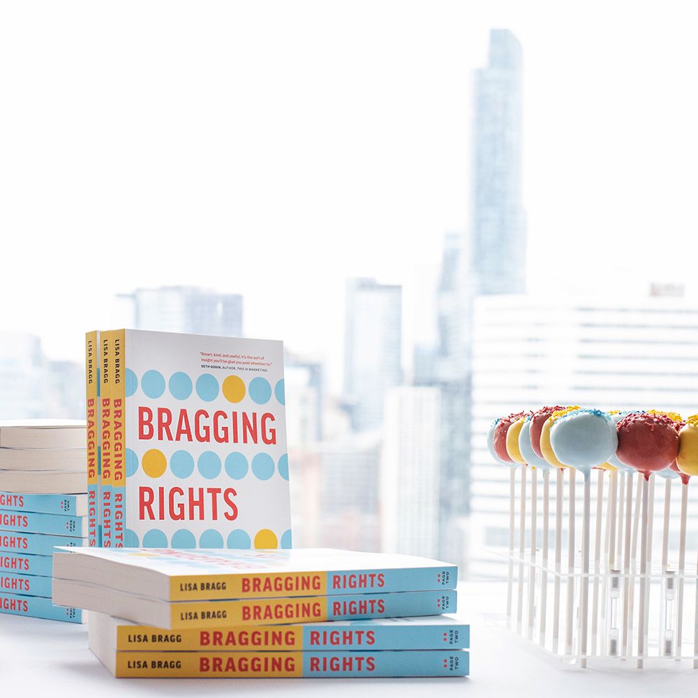 Stack of Bragging Rights books displayed against city skyline backdrop.