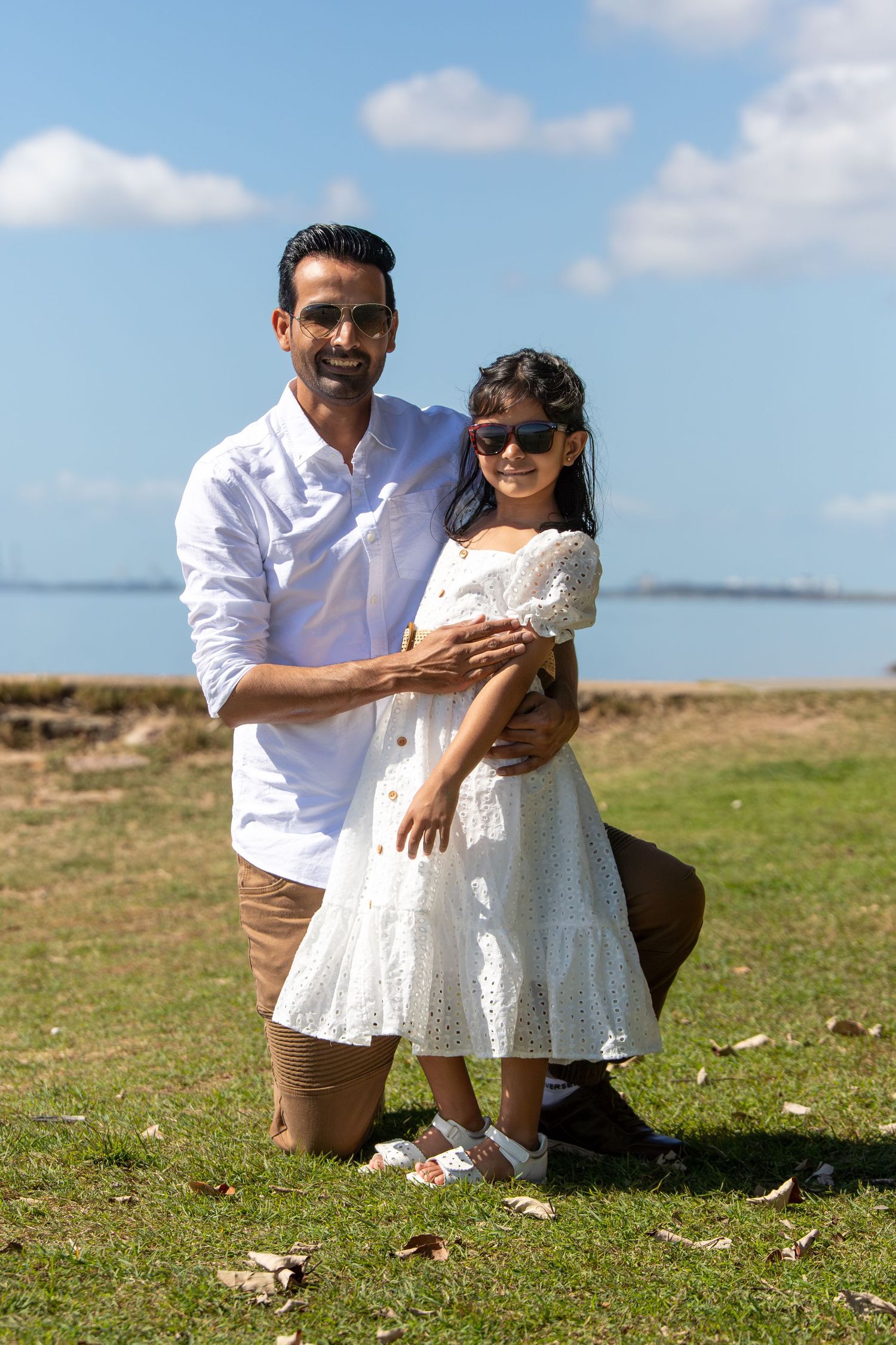 A family in white outfits enjoys a playful moment together on a grassy hillside by the ocean.