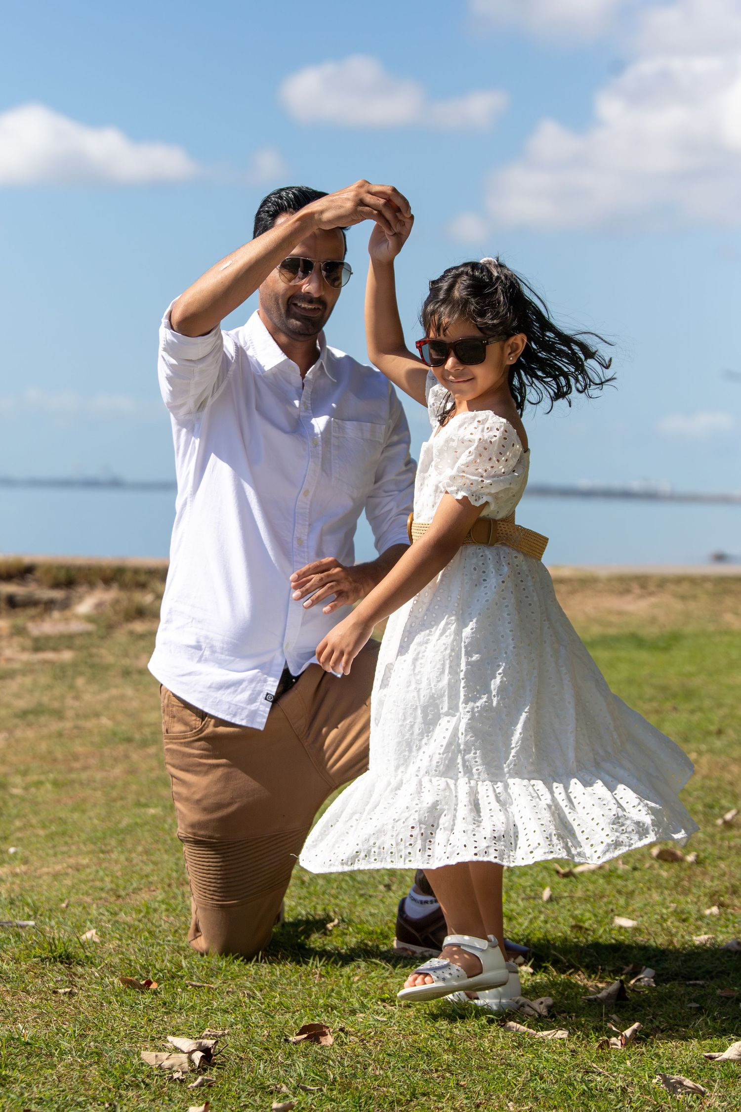 A joyful dance scene unfolds on a grassy coastal area under blue skies.
