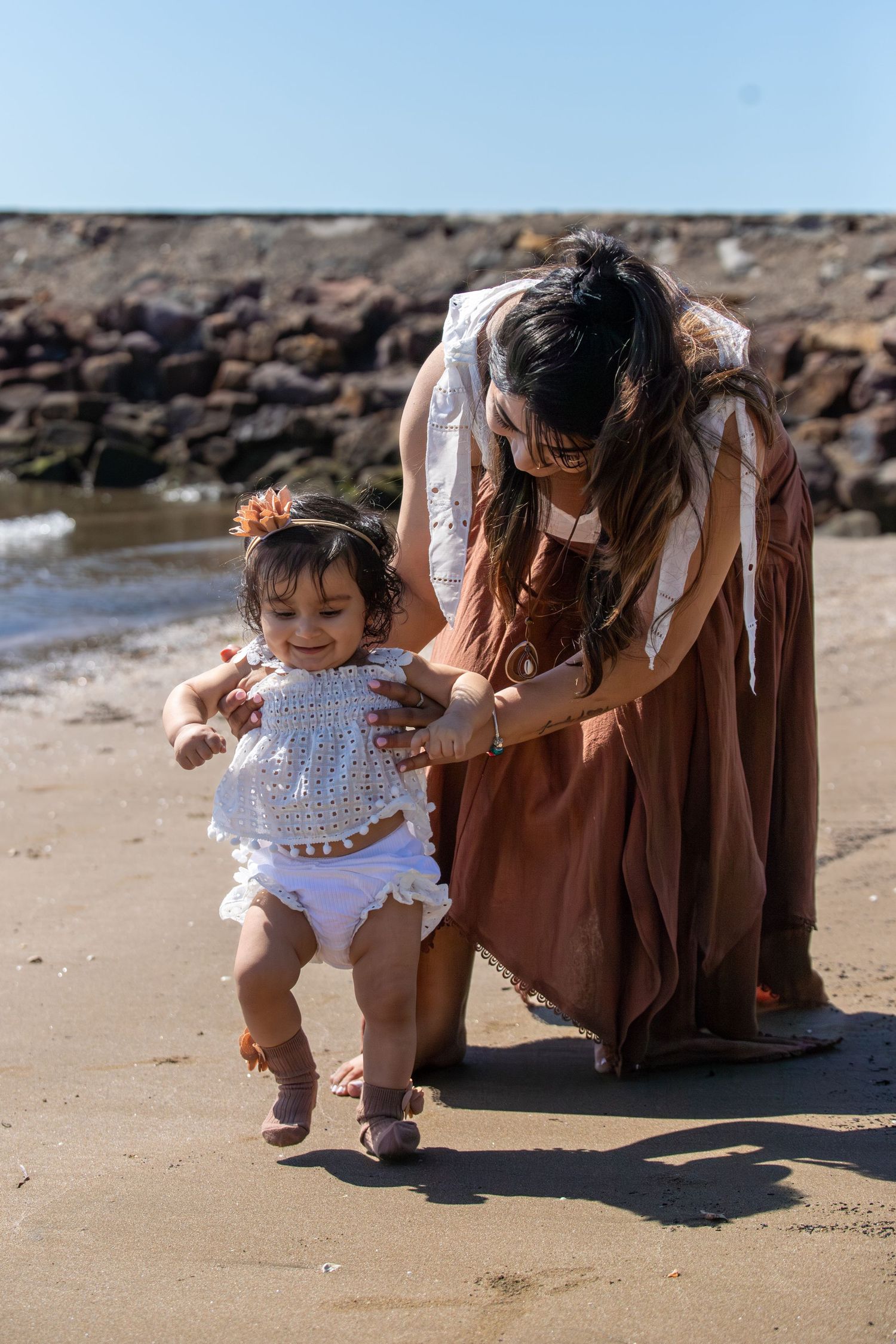 A touching beach scene with a small child in a white dress taking first steps on the sand.