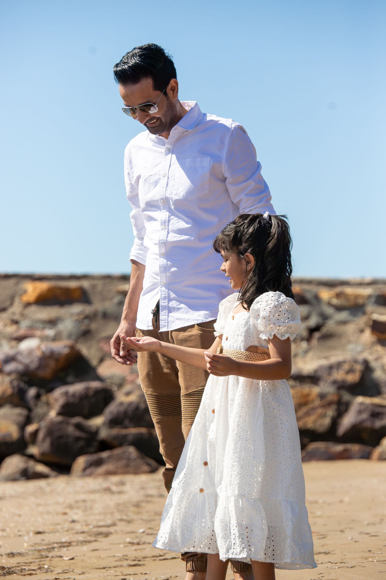 A tender family moment captured against rocky coastal backdrop on a sunny day.