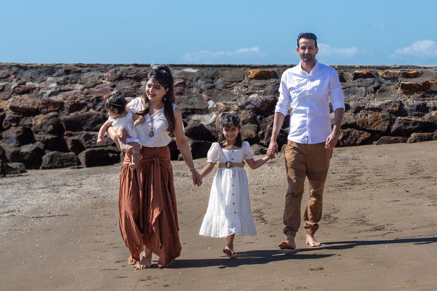 A family strolls together on a sandy beach with rocky outcrops in the background.