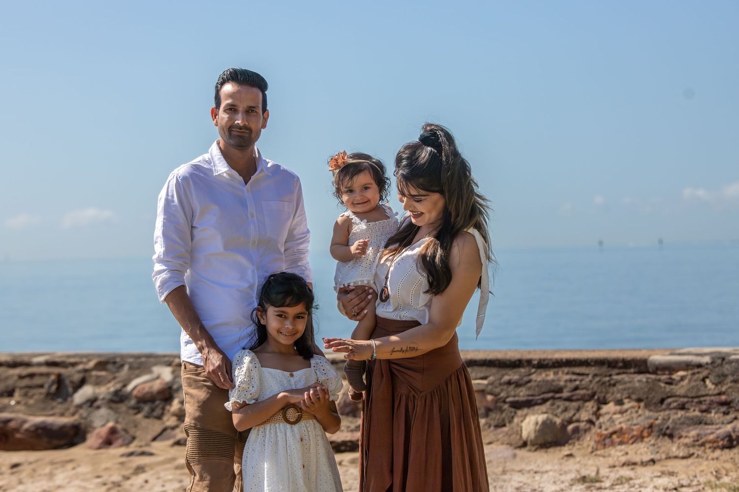 Family enjoying a sunny day together on rocky coastal terrain with ocean views.