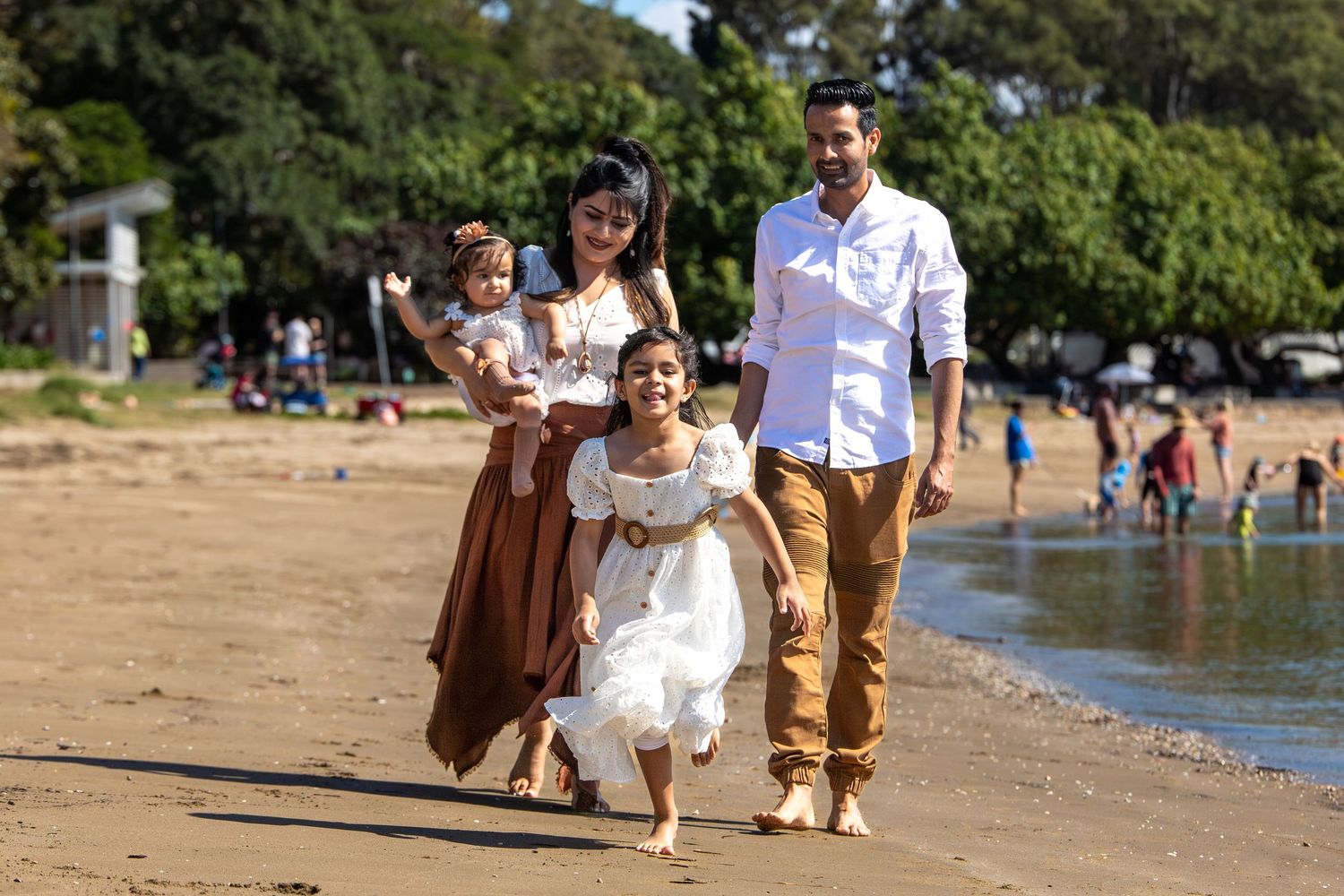 A family shares a fun beach day together near green foliage and blue water.