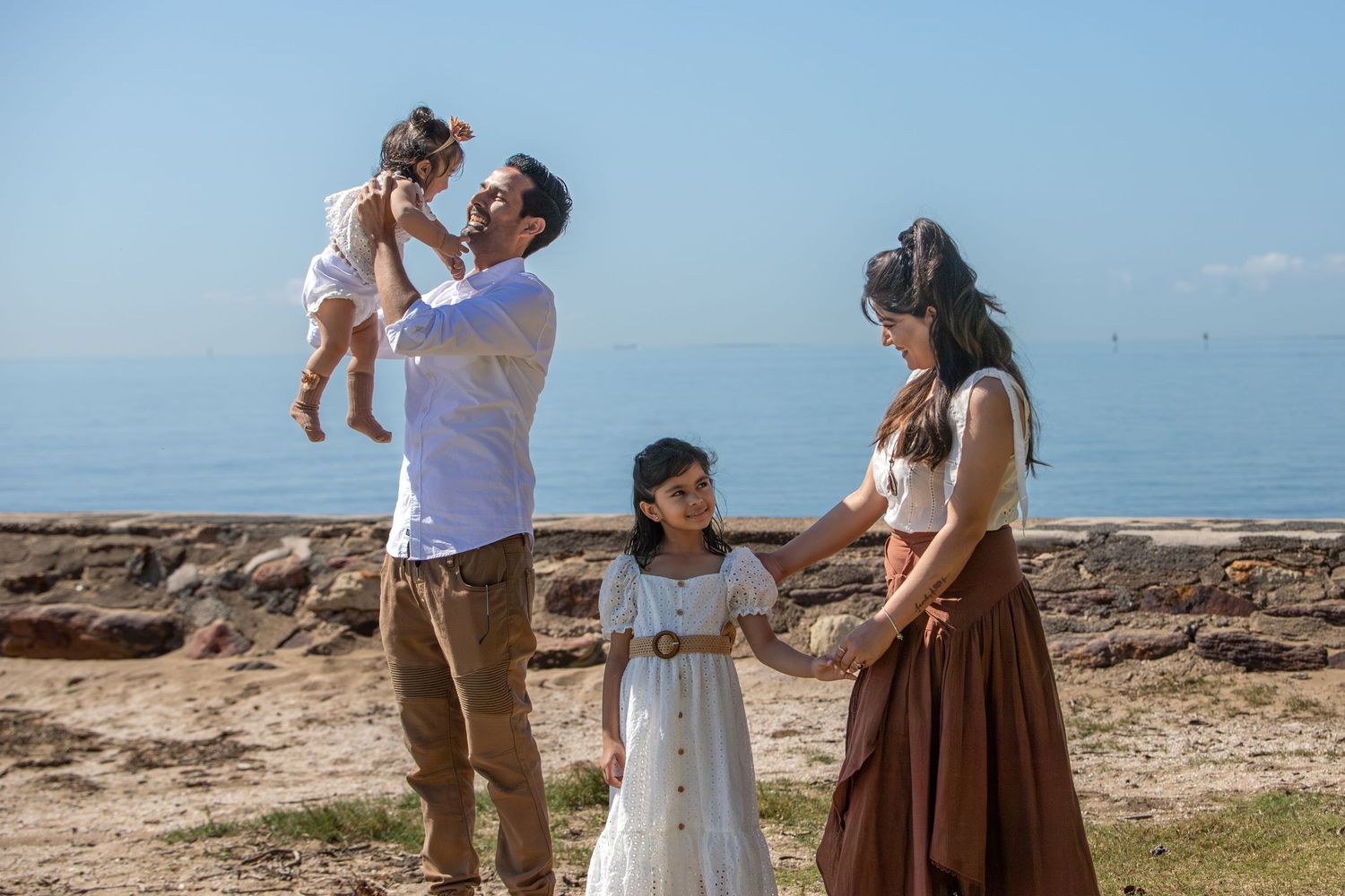 Family playing and laughing together on grassy coastal terrain.