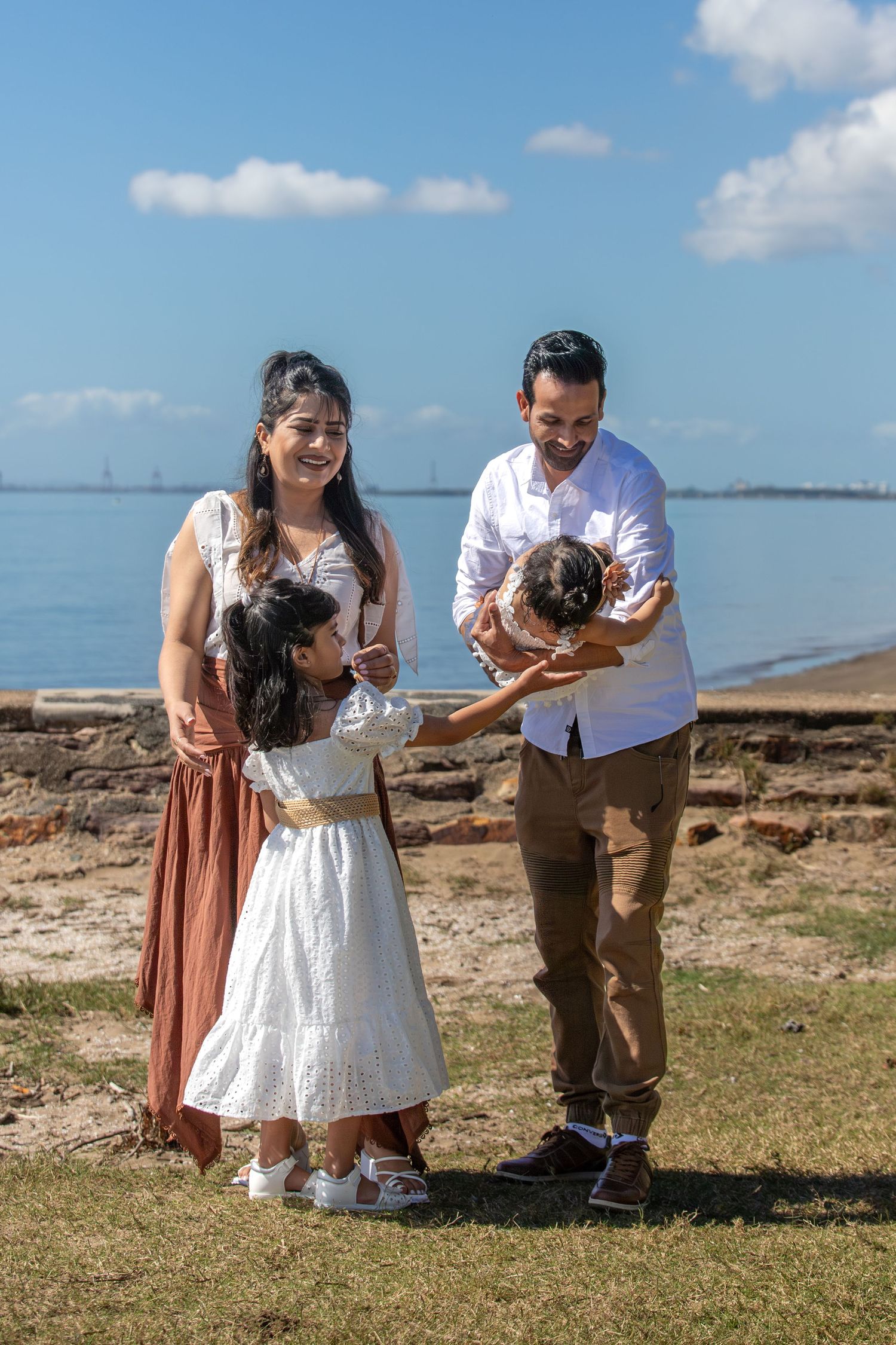 Family bonding moment captured on grassy oceanside cliff under blue skies.