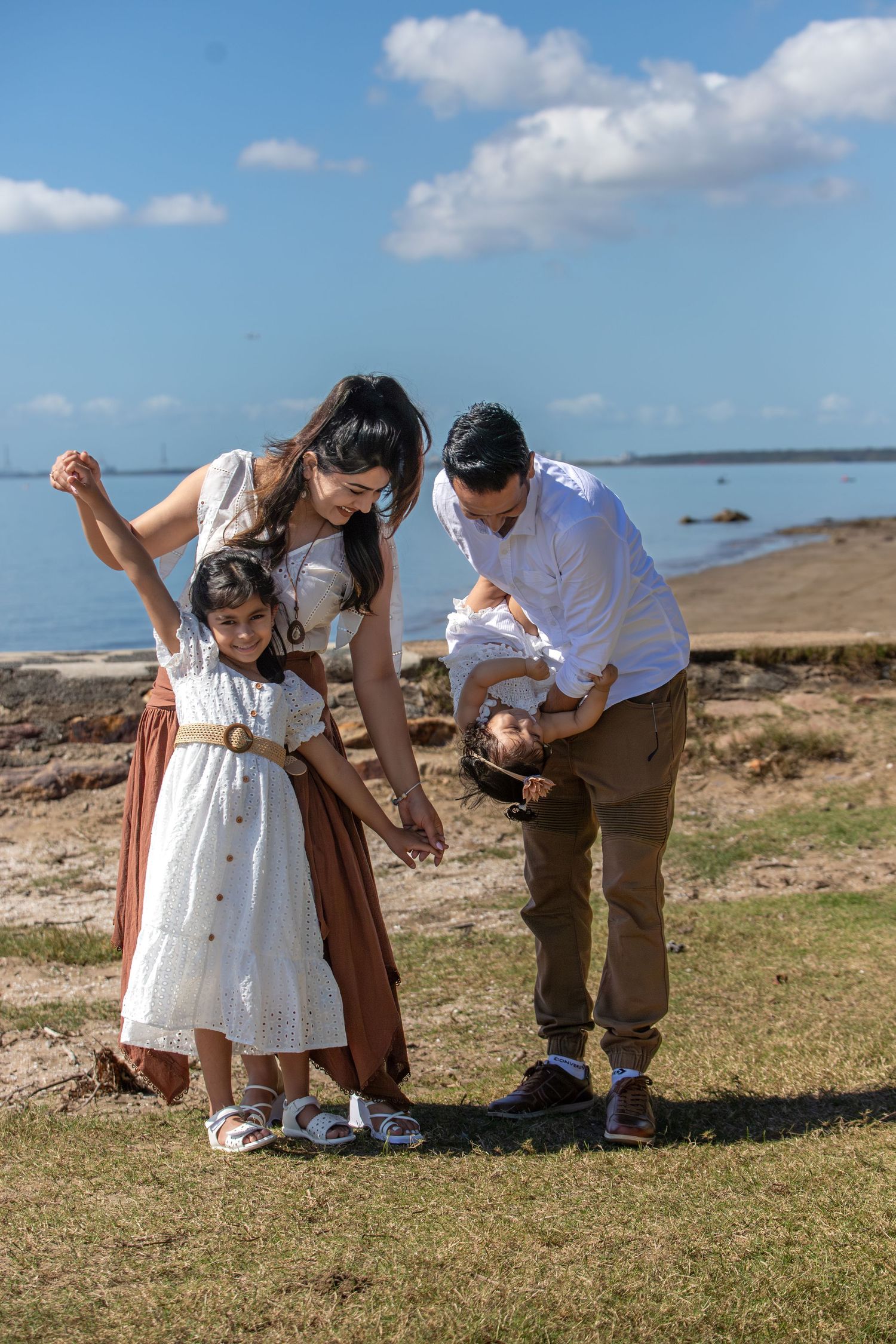 Playful family interaction on coastal grassland with ocean in background.