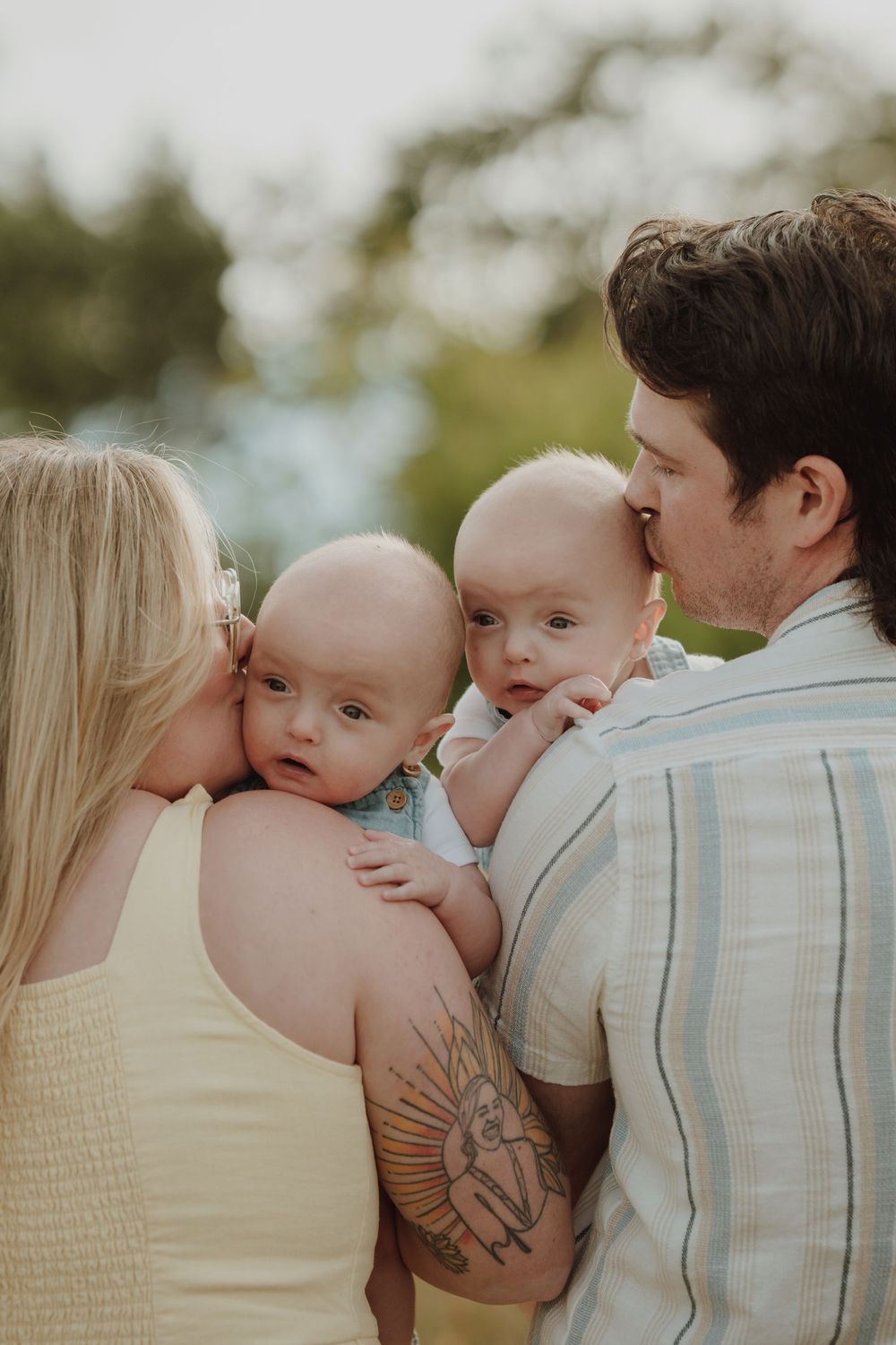Loving parents kissing their twin babies on the cheeks during an outdoor family portrait session in nature in Victoria BC Vancouver Island.