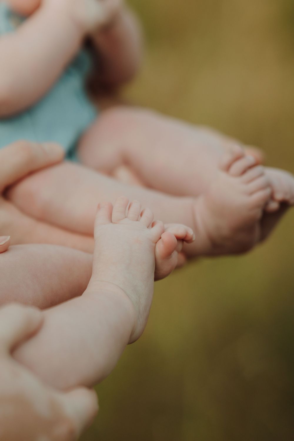 Close-up of two babies holding hands while their tiny feet and legs rest together in a sweet outdoor portrait. In Victoria, BC.