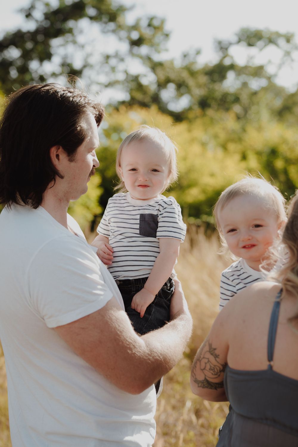 A family with two babies in matching striped shirts enjoying a sunny outdoor moment in a golden field.