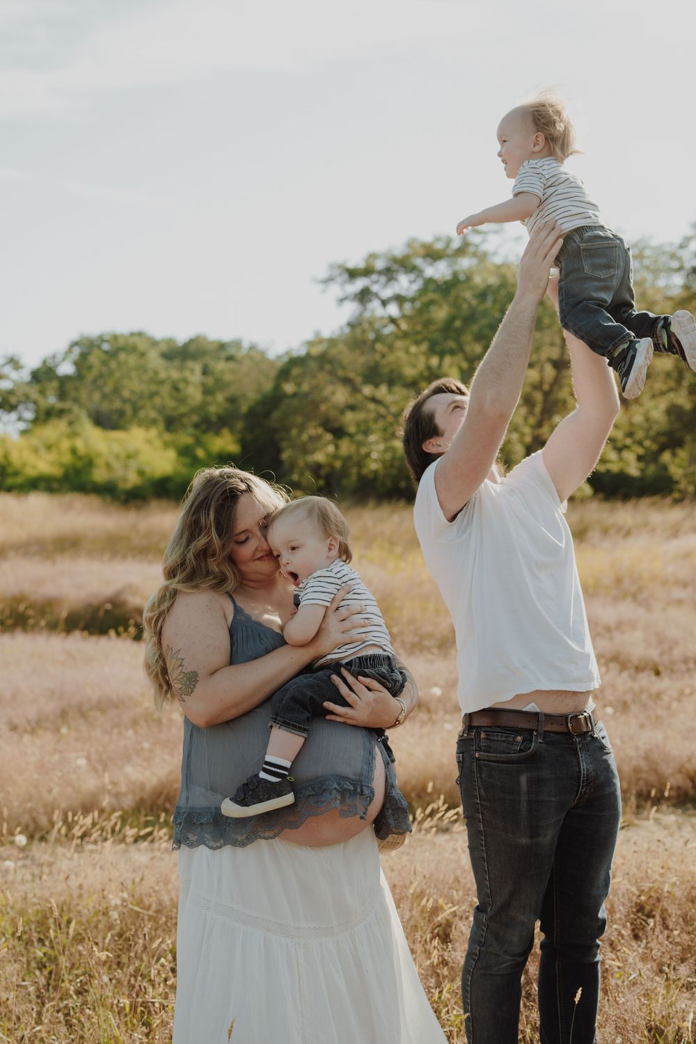 Family of four enjoying a sunny outdoor photo session in a golden field, parents lovingly holding their two young babies.