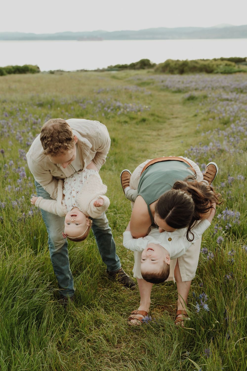 Parents playfully flip their two young children upside down in a blooming wildflower field. Victoria, BC, Vancouver Island.