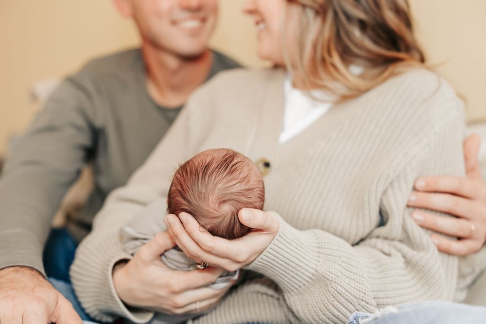 A newborn baby with auburn hair is cradled in soft knit sweaters during an intimate family moment.