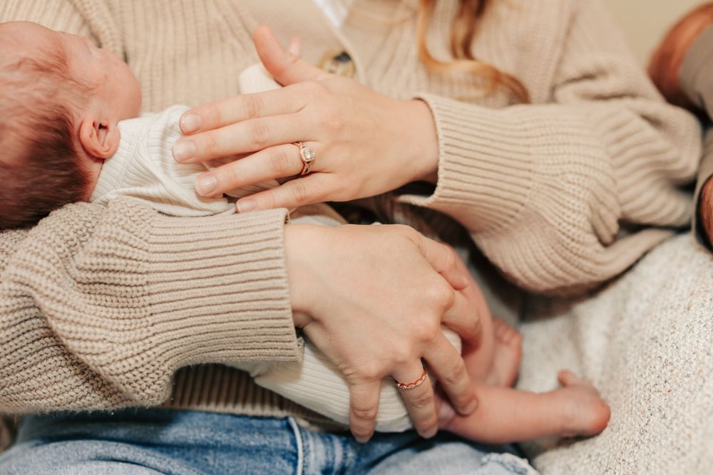Hands in beige knitted sweater sleeves tenderly holding and feeding a baby wrapped in a soft blanket.