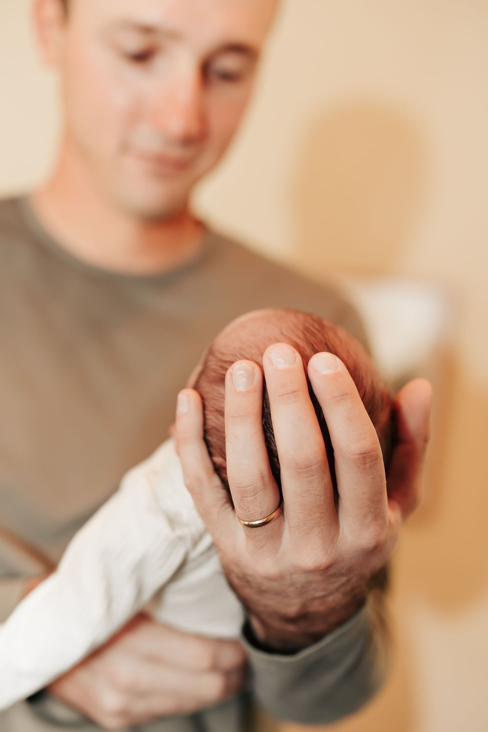 A person wearing a gray shirt gently cradles a tiny newborn baby wrapped in white cloth.