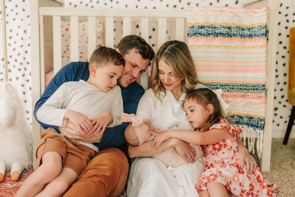 Parents sit with three young children on a cozy bed with twinkling string lights and a patterned tapestry in the background.