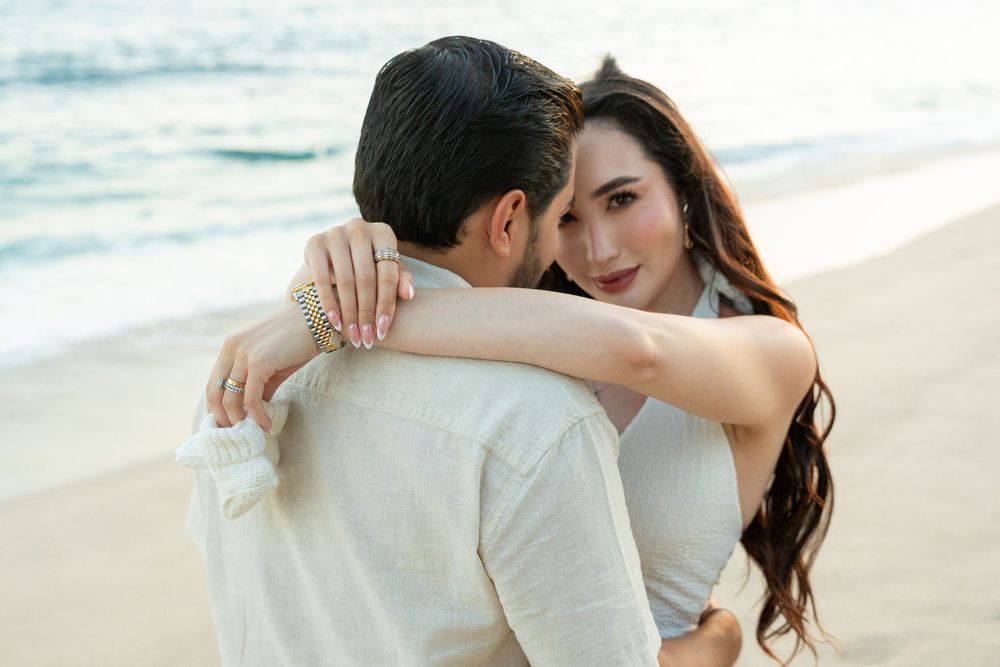 Couple embracing on a beach, woman smiling over man's shoulder, romantic seaside photo session.