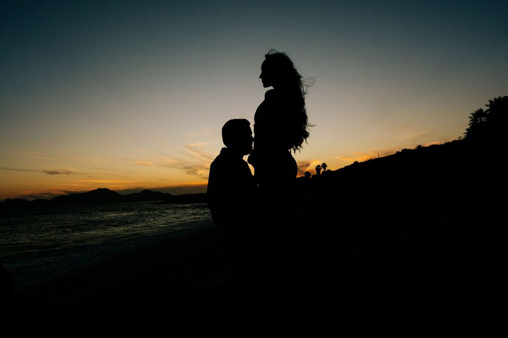 Silhouette of a romantic couple at sunset by the ocean, with warm orange and blue sky in the background.