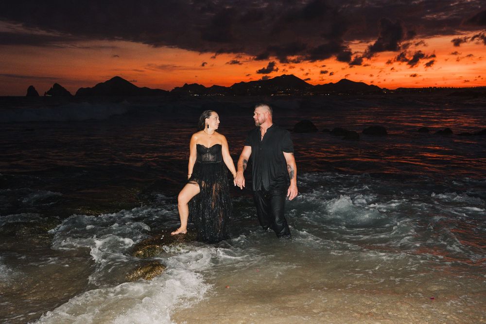 People enjoying a nighttime swim in dark ocean waters against a vibrant orange and purple sunset sky.