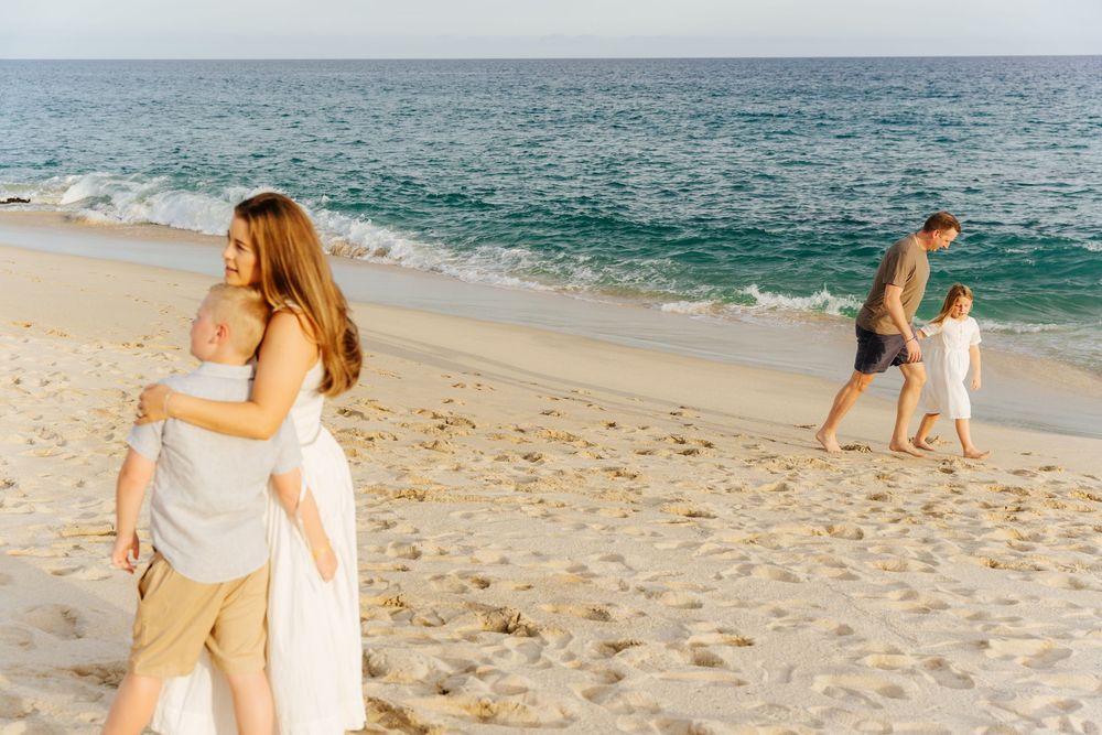 A couple in light colored clothing walks together on a sandy beach with ocean waves in the background.