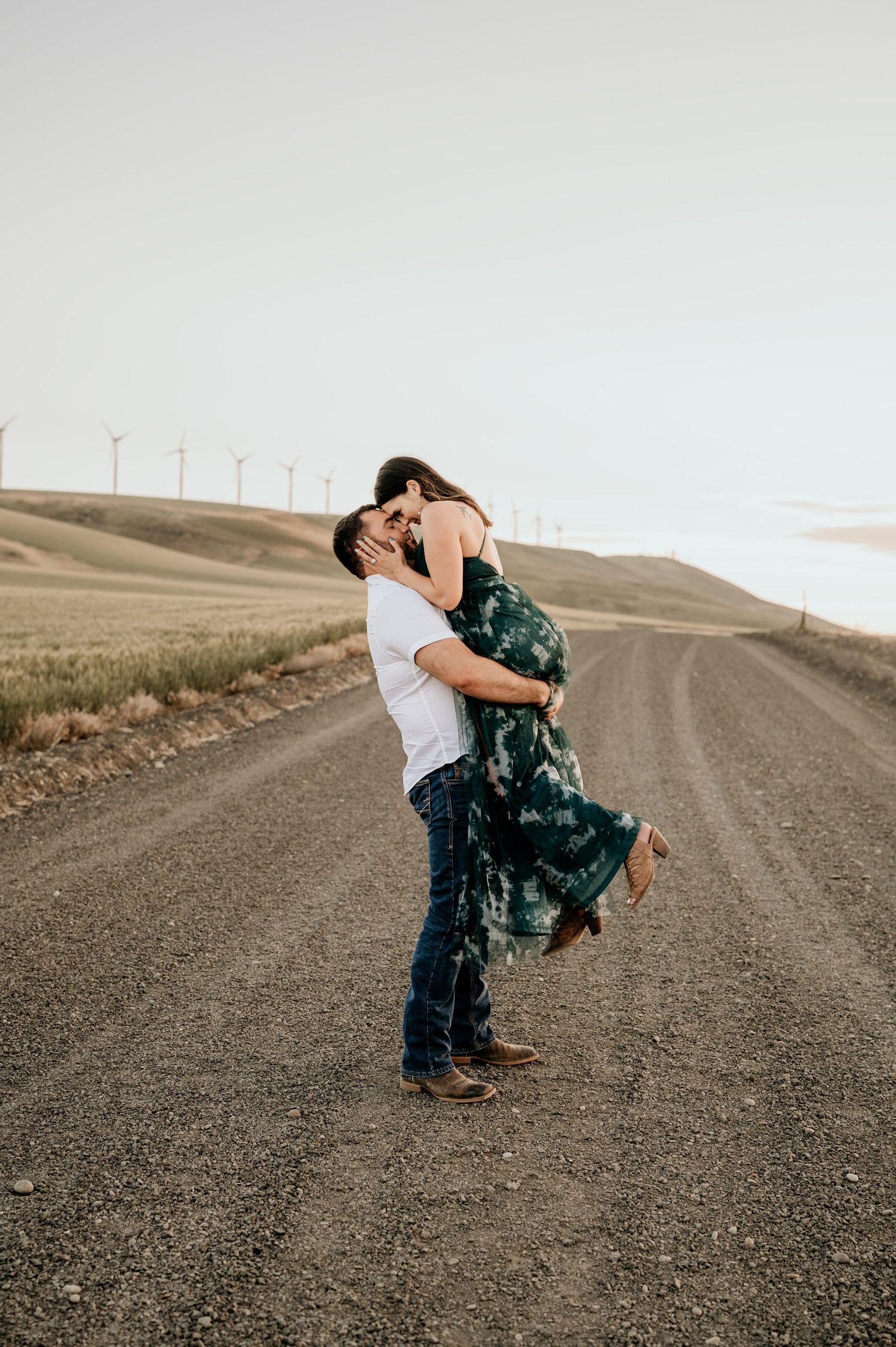 Couple in love on a dirt road surrounded by windmills for their engagement photos.