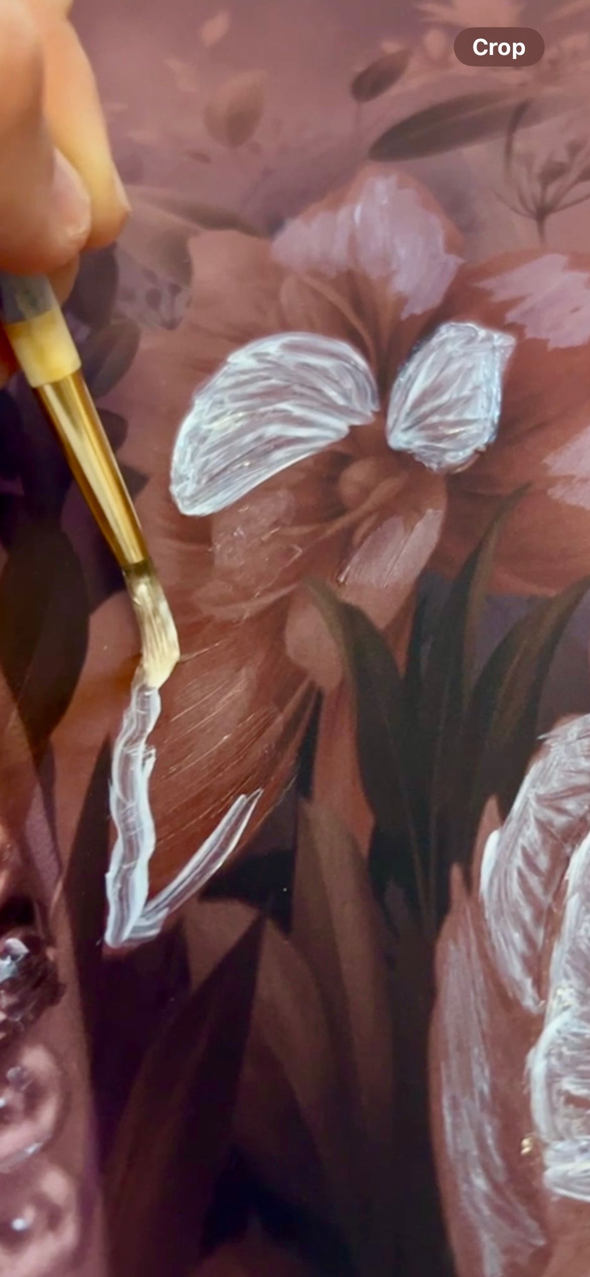 A paintbrush mixes colors on an artist's palette with red, yellow and white paint visible in the background custom painting artwork