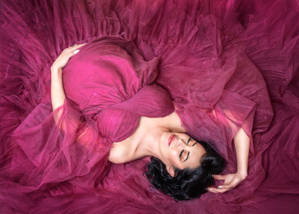 A figure in a dramatic flowing fuchsia tulle gown lays gracefully against a dark pink background.