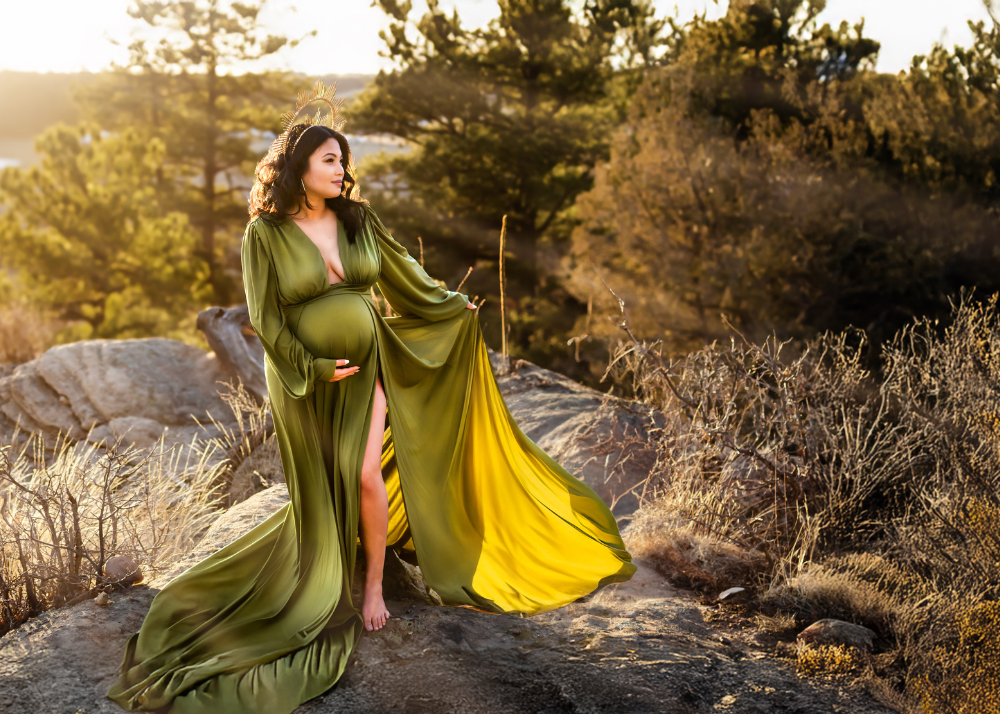 Flowing olive green and yellow dress billows in the wind against rocky mountain terrain at golden hour sunset.