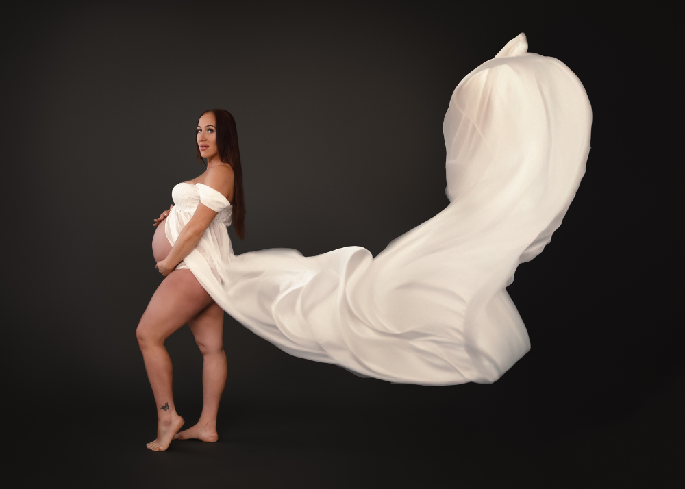 Elegant maternity photo featuring flowing white fabric dramatically billowing against dark backdrop.